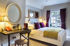 A bedroom with a bed, a desk with a lamp, a chair, a mirror, and a window with curtains. - The Chequers Marlow (Marlow)