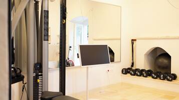 A gym with exercise equipment, a mirror, a computer monitor, and a row of dumbbells.
