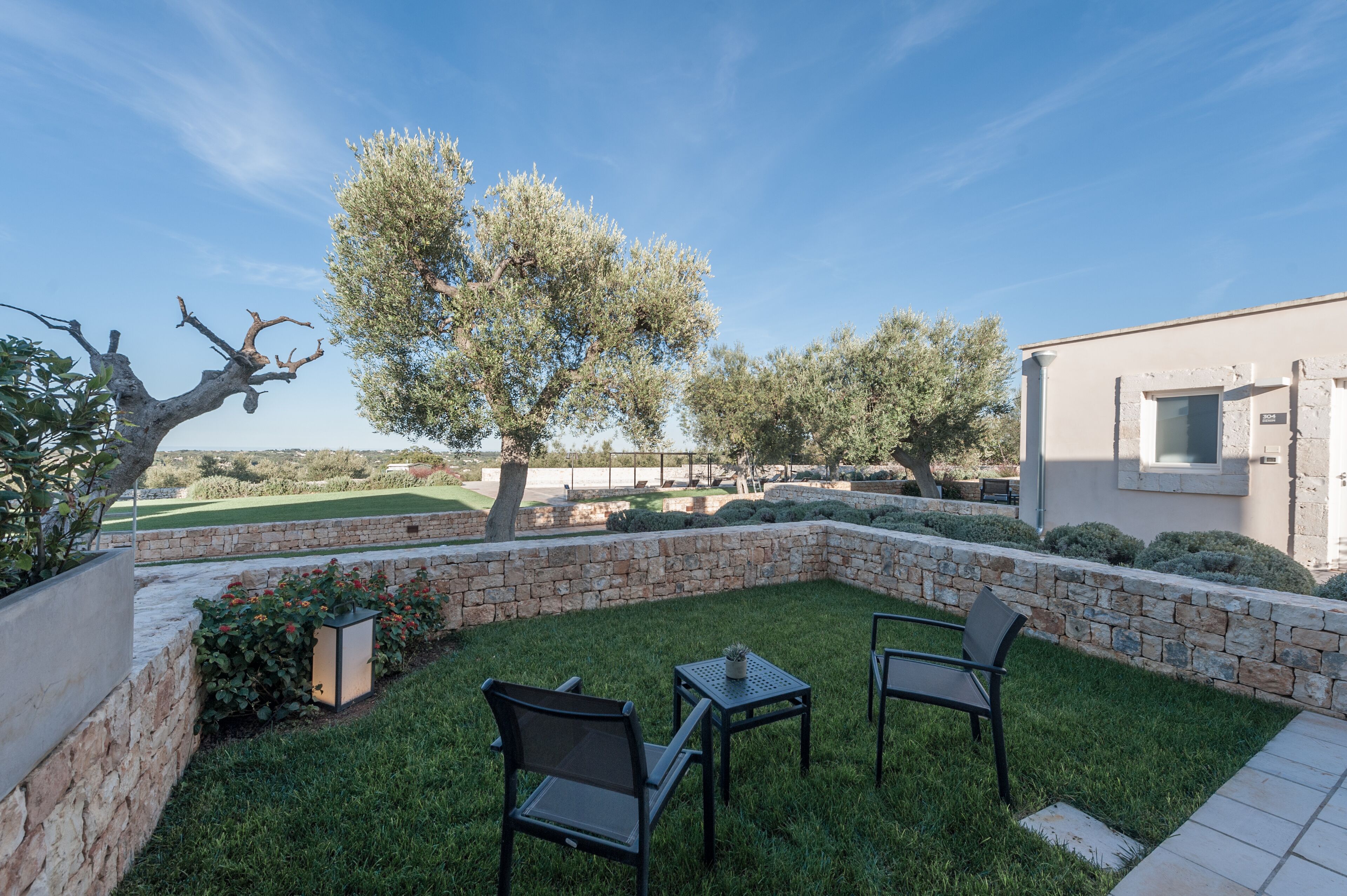 Un patio con muros de piedra, césped y un edificio con ventana.