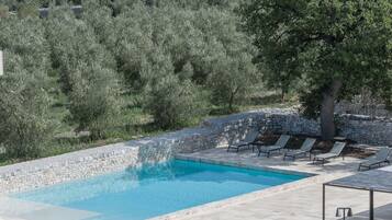 A swimming pool with stone walls and lounge chairs.