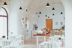 Zona pranzo con tavoli e sedie bianche, lampade a sospensione nere e un tavolo buffet in legno.