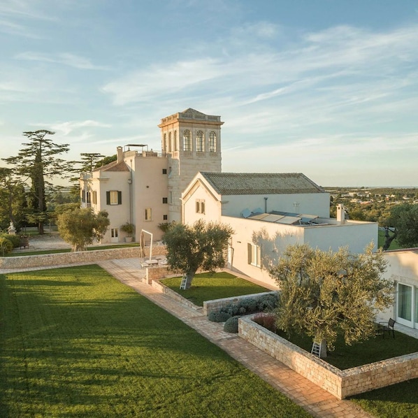 Un grand bâtiment blanc, doté d’une tour, entouré d’une pelouse bien entretenue et de murs en pierre.