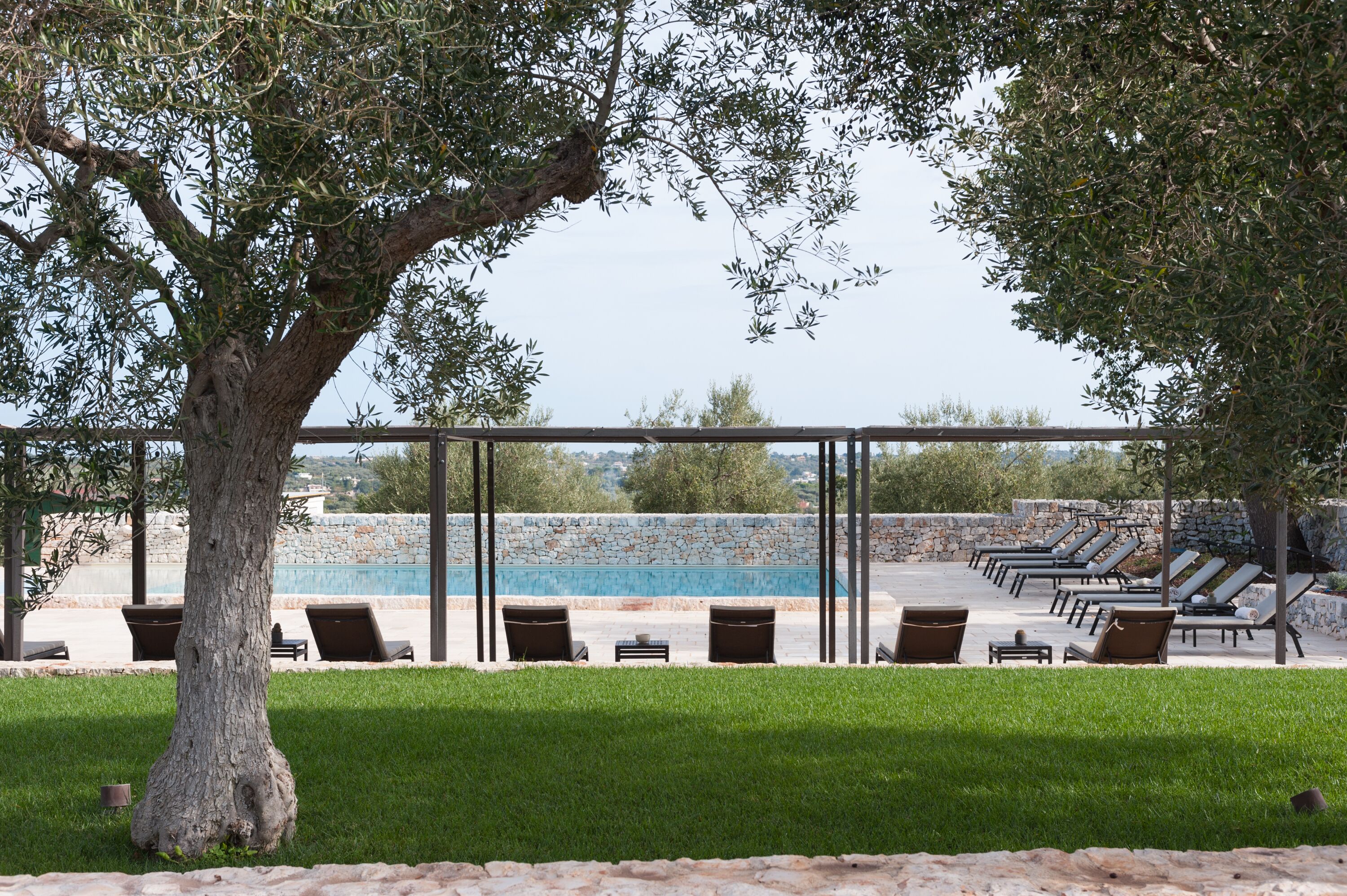 Un área junto a la piscina con sillas de descanso y una pared de piedra.