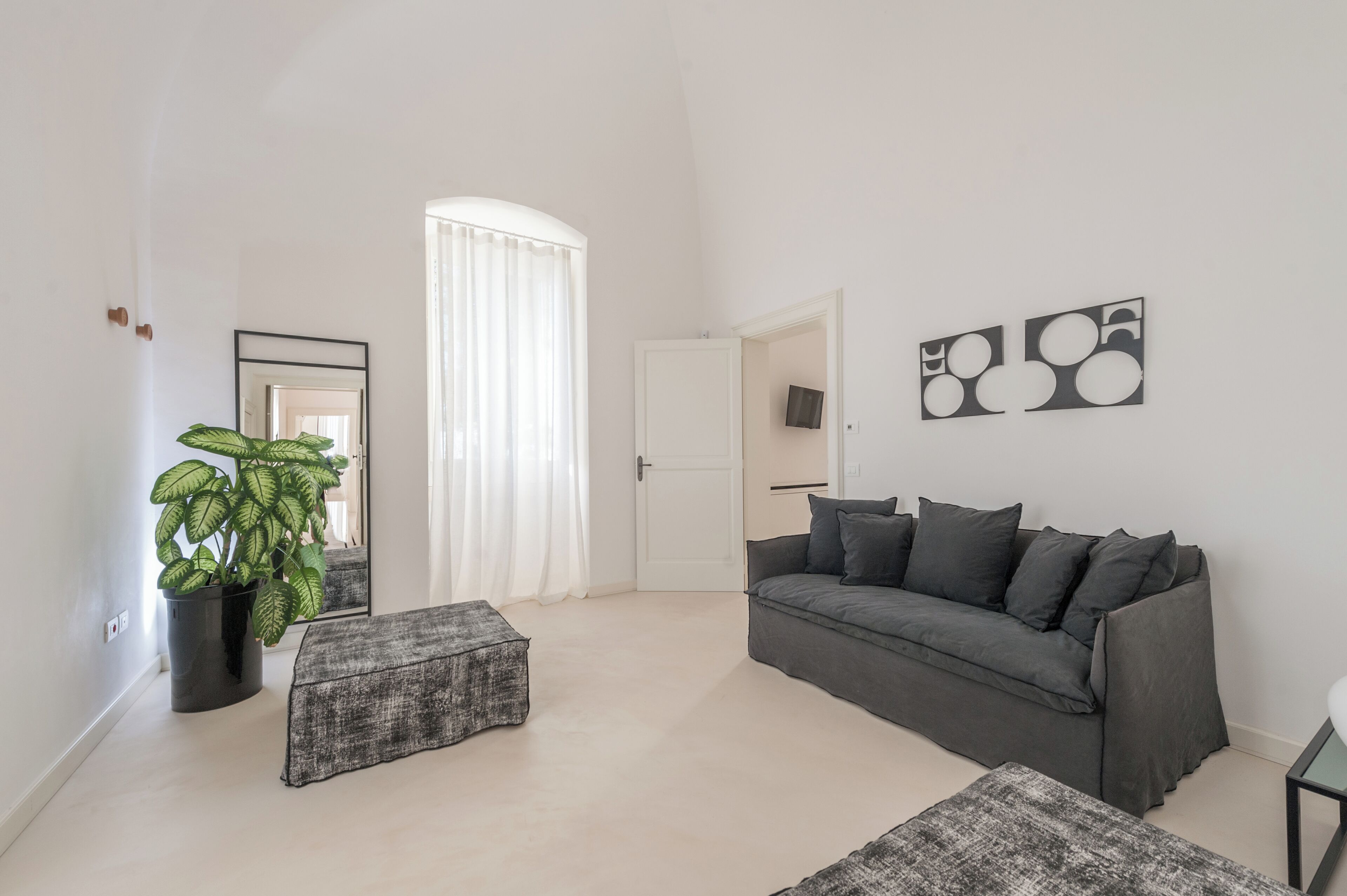 Un salón moderno con un sofá gris, una mesita, una planta en maceta y un gran ventanal con cortinas blancas.