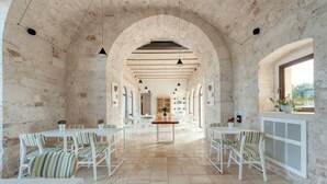 Un interior espacioso con paredes de piedra, muebles blancos y una mesa central.