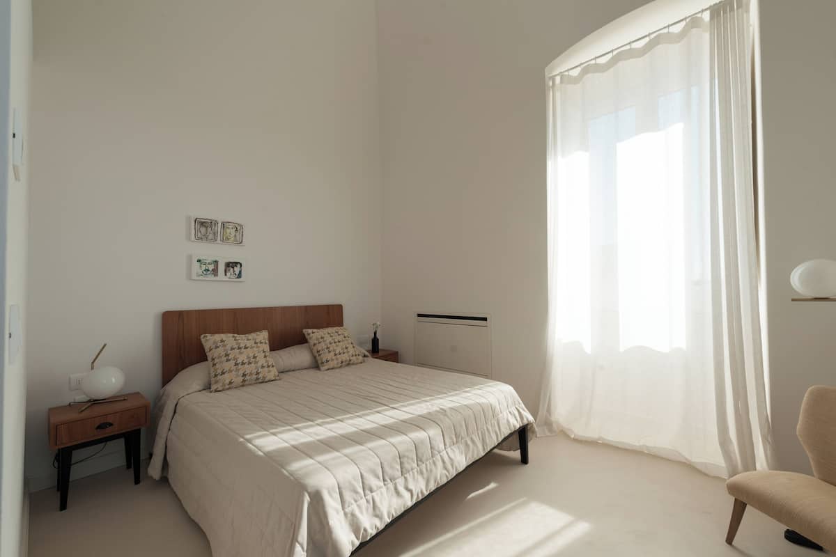 A bedroom with a bed, a nightstand, a lamp, and a chair.