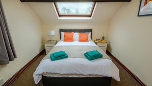 Un dormitorio con tragaluz, una cama con ropa de cama blanca y naranja, dos mesitas de noche y una mesita de noche con una lámpara.