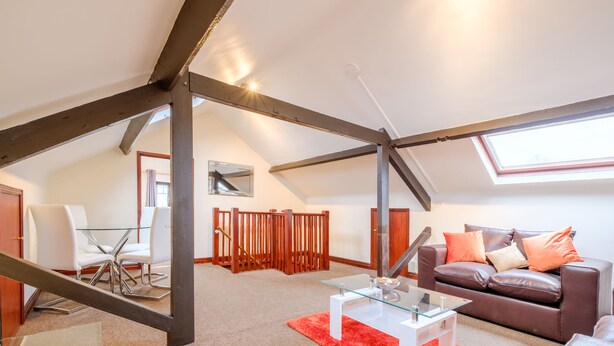 Un loft espacioso con techo alto, vigas de madera a la vista, una mesa de vidrio, un sofá de cuero y una alfombra roja.