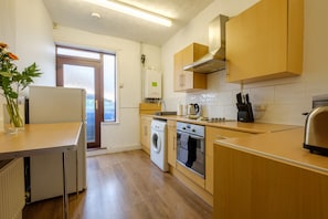 A modern kitchen with wooden cabinets, a built-in oven, a washing machine, and a window with a view. - City Road Apartment (Norwich)