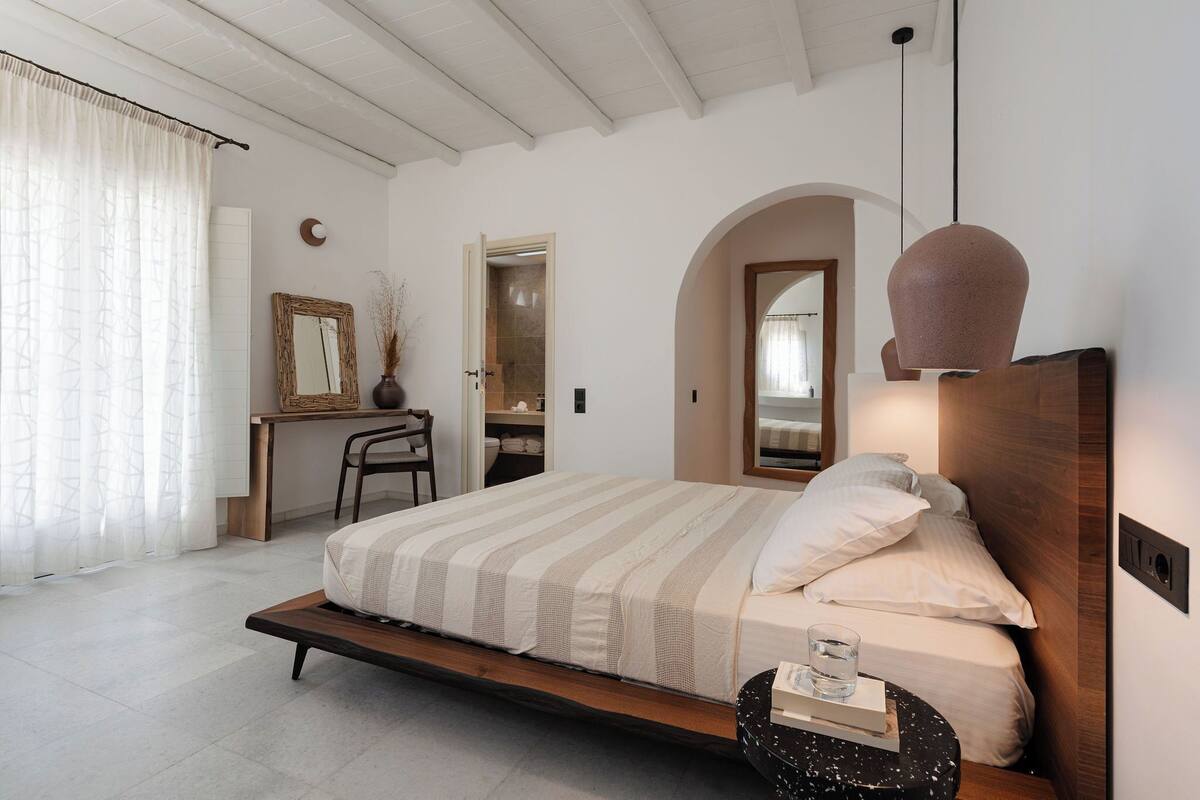 A bedroom with a bed, bedside table, chair, and a desk with a mirror.