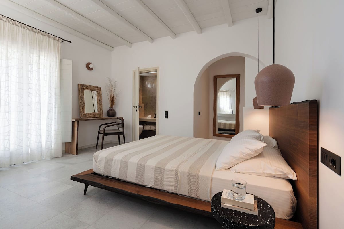Un dormitorio con cama, mesita de noche, silla y escritorio con espejo.