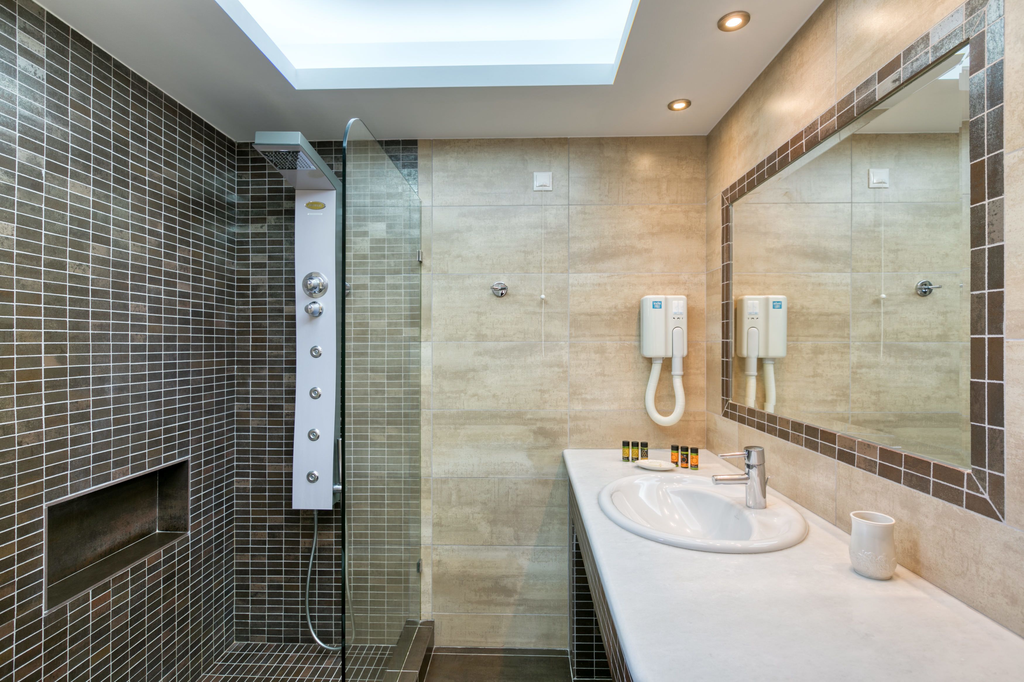 Une salle de bain moderne dotée d’une lucarne, d’une douche à parois de verre, d’un lavabo avec un miroir et d’un porte-serviettes.