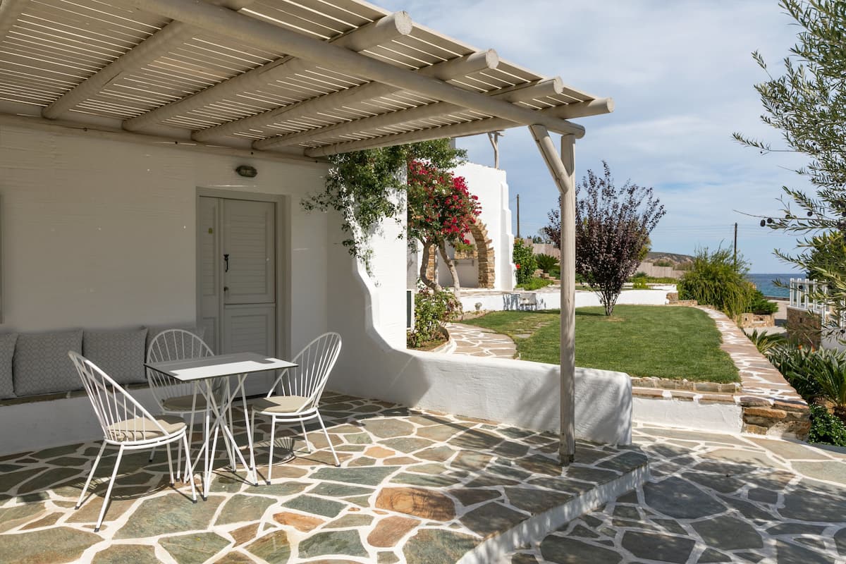 A covered patio with stone flooring, a white table with chairs, and a view of the sea.