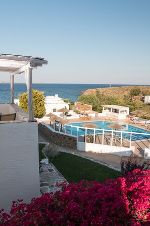 A pool area with a view of the sea, surrounded by white buildings and greenery.