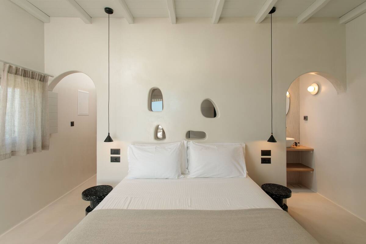 A minimalist bedroom with a large bed, two bedside tables, a mirror, and a small seating area.