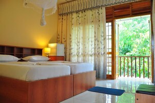 Un dormitorio con cama, lámpara de noche, cortinas y vistas a vegetación a través de una puerta abierta.