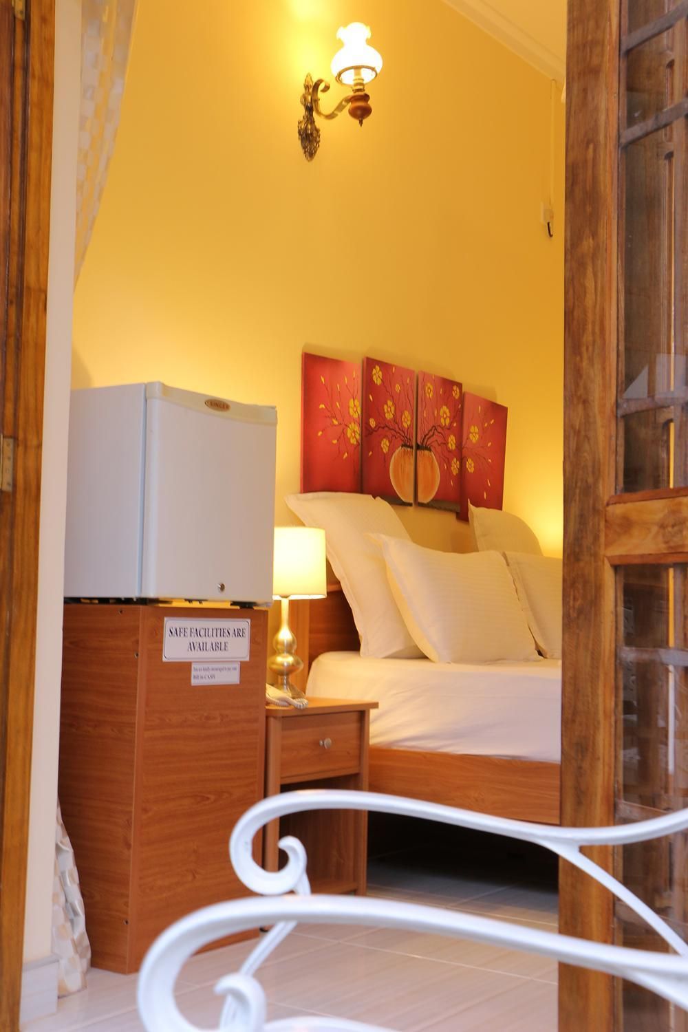 Une chambre d’hôtel équipée d’un lit, d’une table de chevet, d’une lampe, d’un luminaire fixé au mur et d’un panneau indiquant la présence d’installations sanitaires accessibles et sûres.