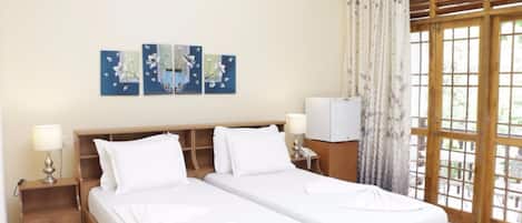 Habitación de hotel con dos camas, cabecero de madera, mesita de noche con lámpara, televisor y ventana grande con cortinas.