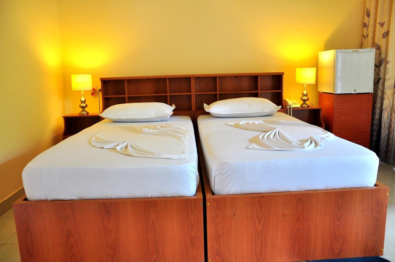 Habitación de hotel con dos camas, cabeceros de madera, ropa de cama blanca y lámparas de noche.