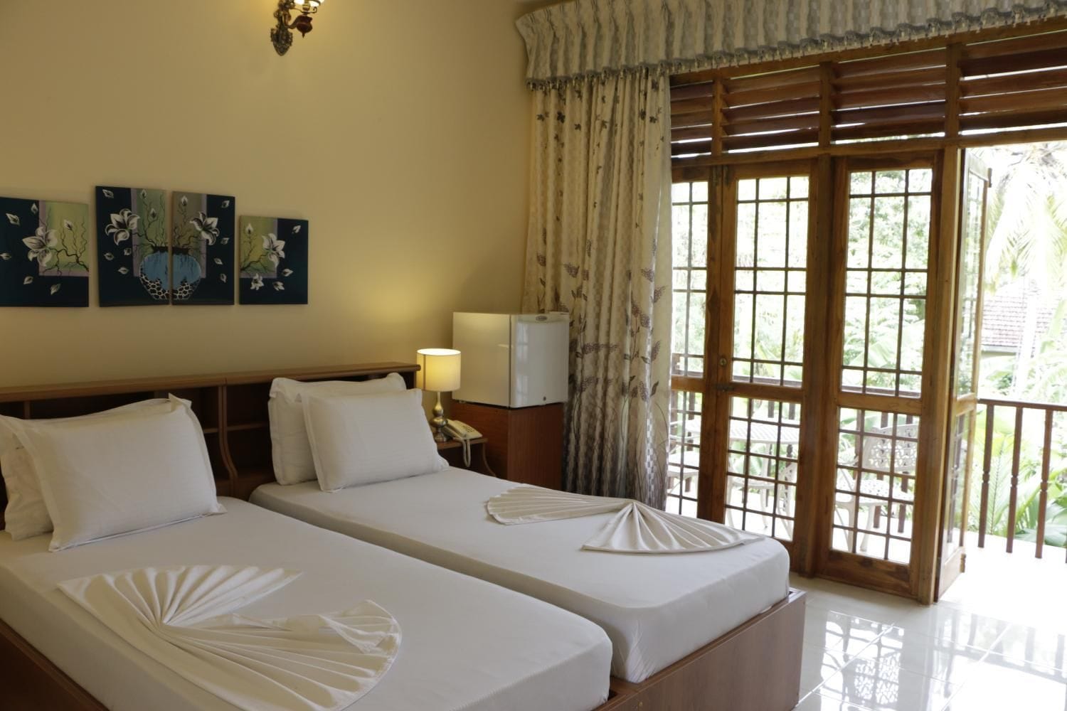 A hotel room with two beds, a nightstand with a lamp, and a window with curtains.