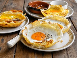 Un plato de desayuno con un huevo dentro de un bol de pan, acompañado de un recipiente pequeño con salsa.