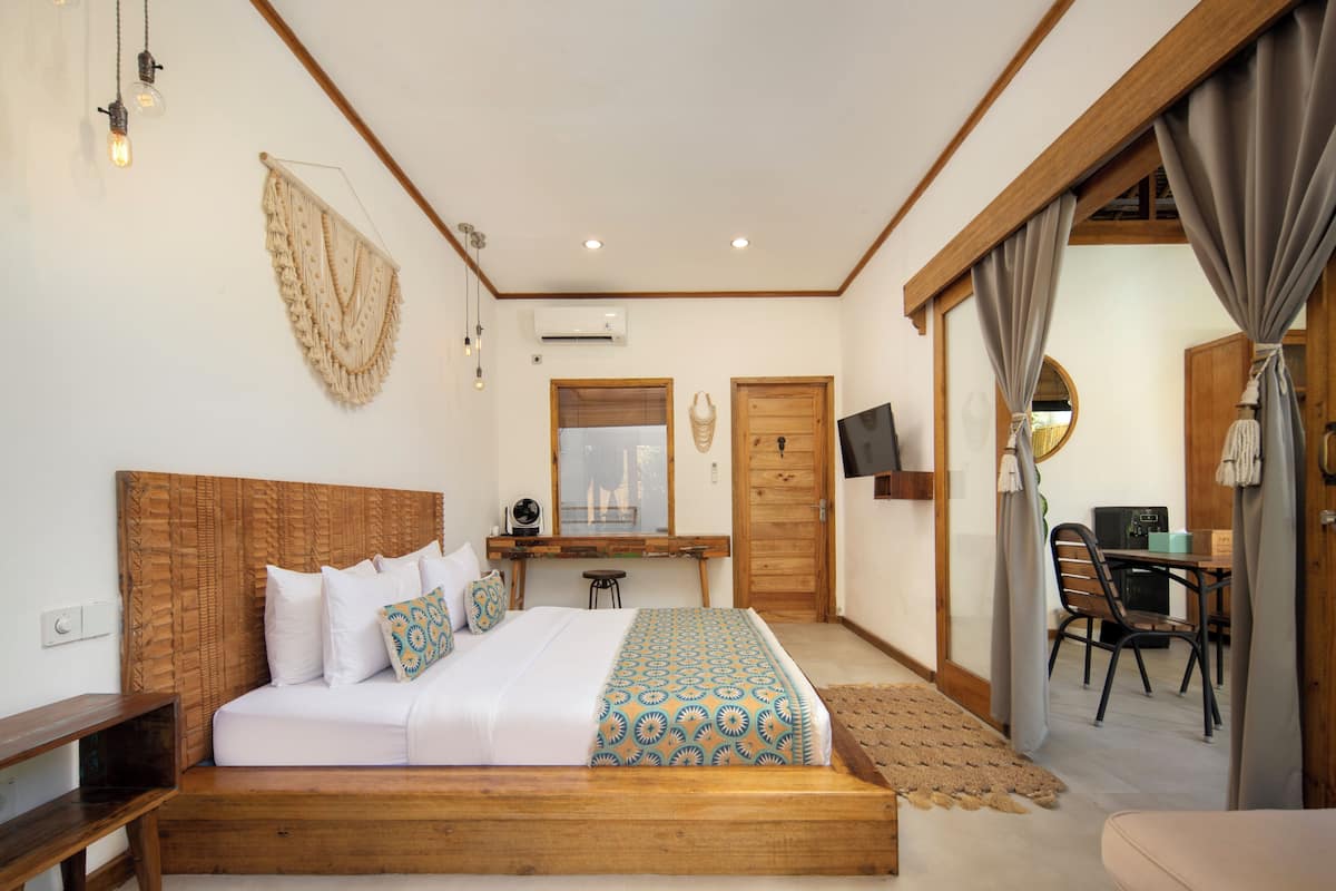 A bedroom with a wooden headboard, a bed with patterned bedding, a desk with a chair, and a TV mounted on the wall.