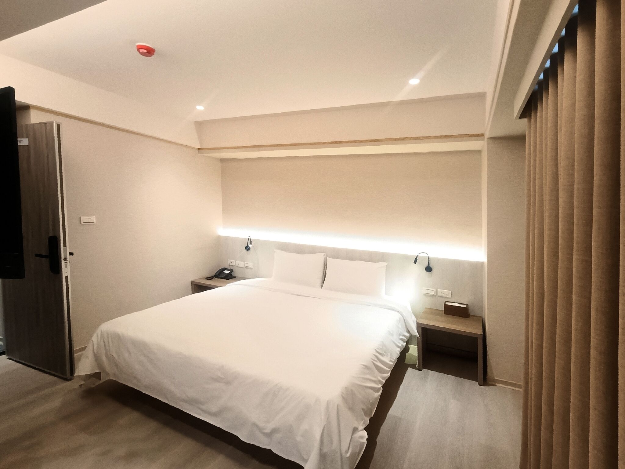 A modern hotel room with a large bed, bedside tables, a desk, and a wardrobe.