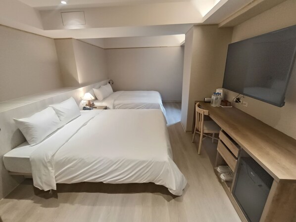 A hotel room with two beds, a desk, a television, and a small table with water bottles. - Good Hotel (Kaohsiung)