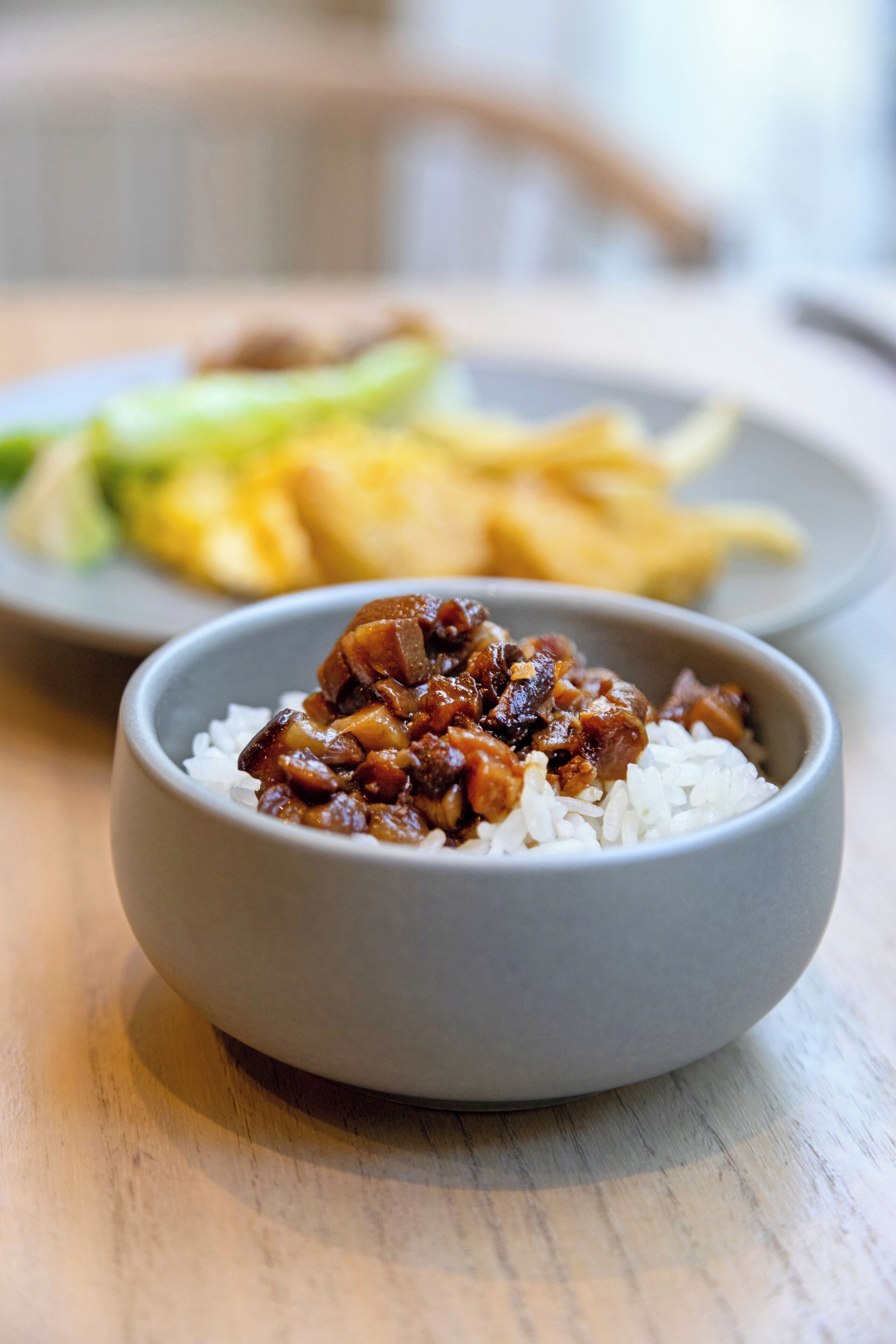 Un tazón de arroz con un plato de carne, acompañado de una fuente de verduras y un tazón de comida amarilla.