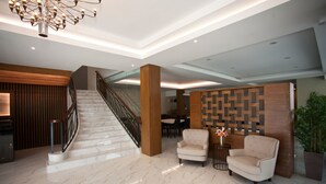 A spacious lobby with a marble staircase, a reception desk, and two armchairs.