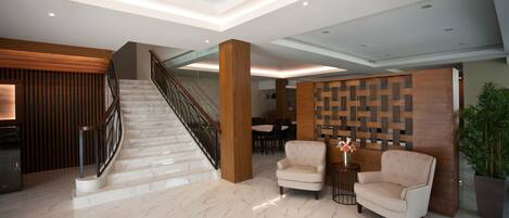A spacious lobby with a marble staircase, a reception desk, and two armchairs.