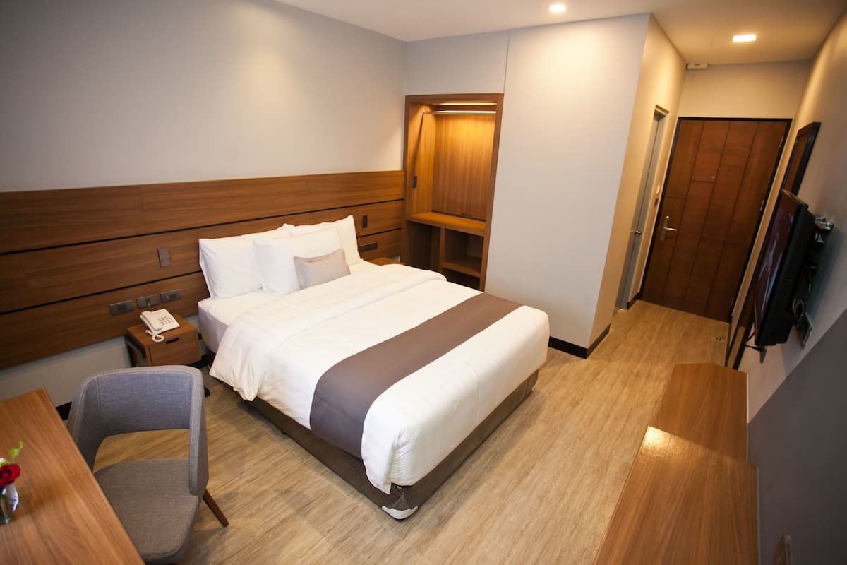 Habitación de hotel con una cama grande, un escritorio con silla, una mesita de noche, un teléfono y un armario.