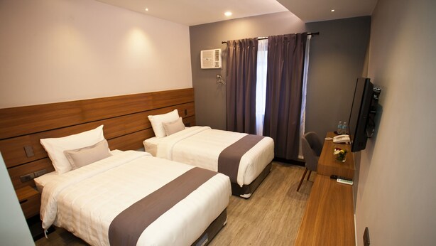 A hotel room with two beds, a desk, a chair, a TV, and an air conditioning unit.