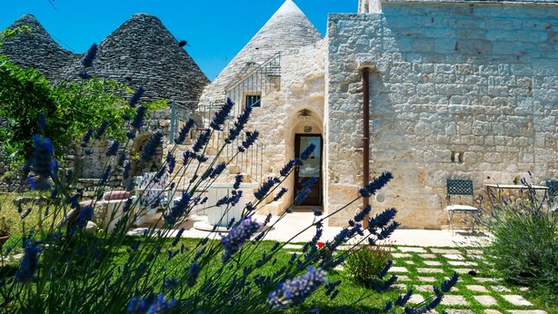 A stone building with a conical roof, a doorway, and a small table with chairs outside. - Trulli Donna Isabella (Locorotondo)