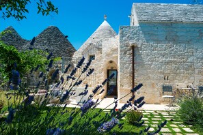 A stone building with a conical roof, a doorway, and a small table with chairs outside. - Trulli Donna Isabella (Locorotondo)