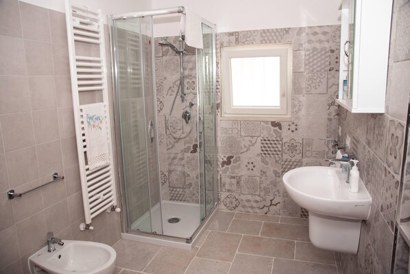 Une salle de bain avec une douche à parois de verre, un lavabo sur colonne et un petit bidet.