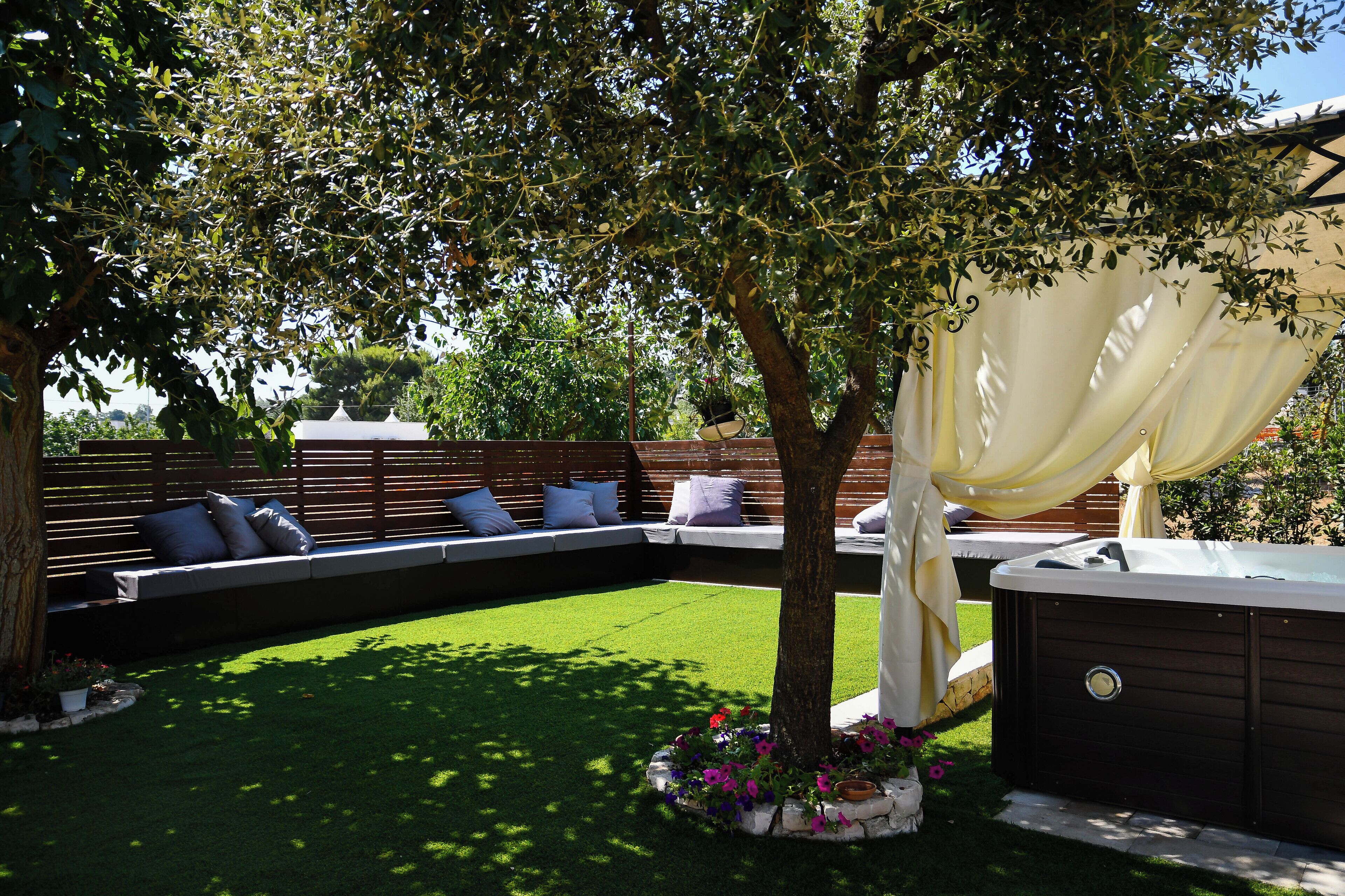 Un jardin avec un jacuzzi, une terrasse en bois et un coin salon avec des coussins.