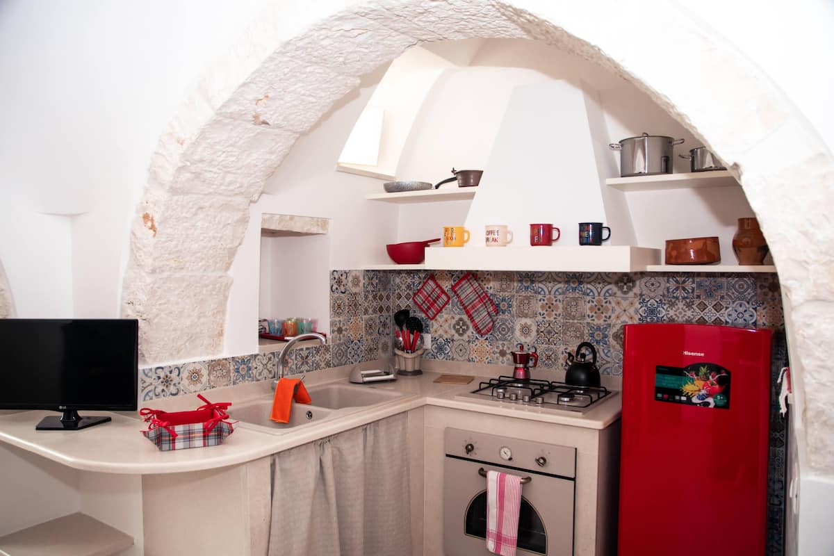 A compact kitchen with white cabinetry, a red refrigerator, and a tiled backsplash.