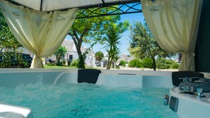A hot tub with a view of a garden and buildings in the background. - Trulli Donna Isabella (Locorotondo)