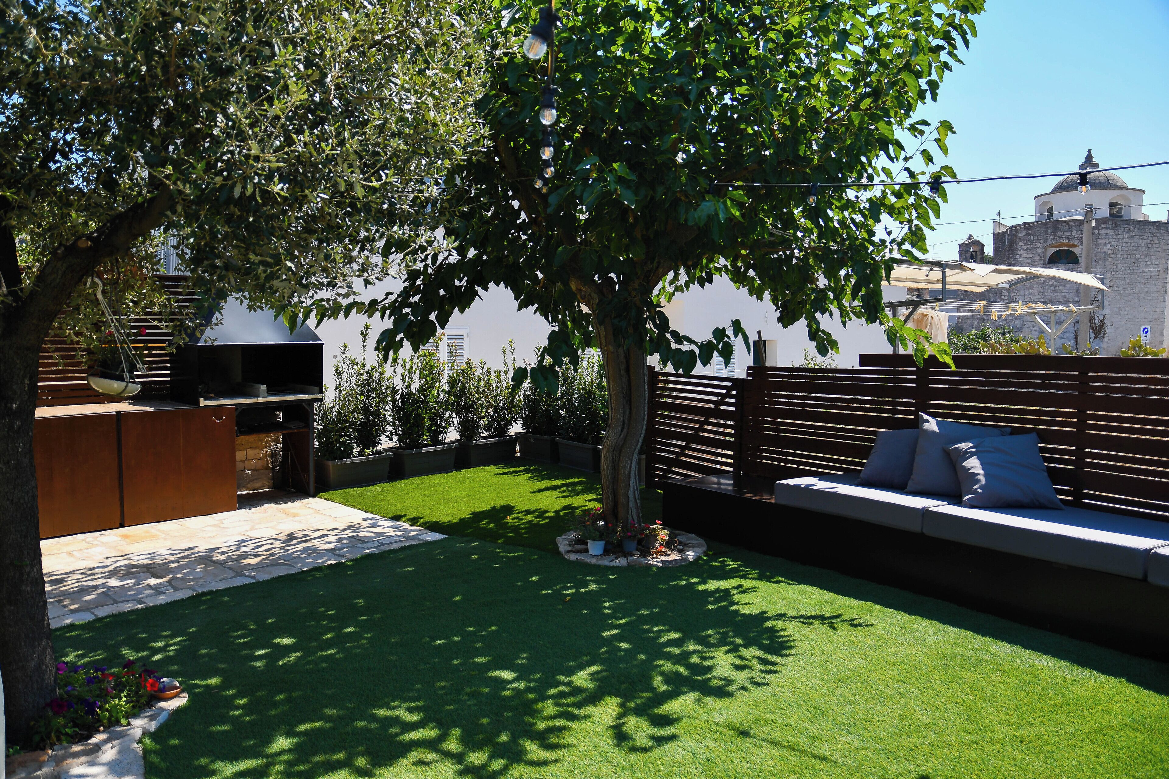 A backyard with a barbecue area, a seating area with cushions, and a tree providing shade.
