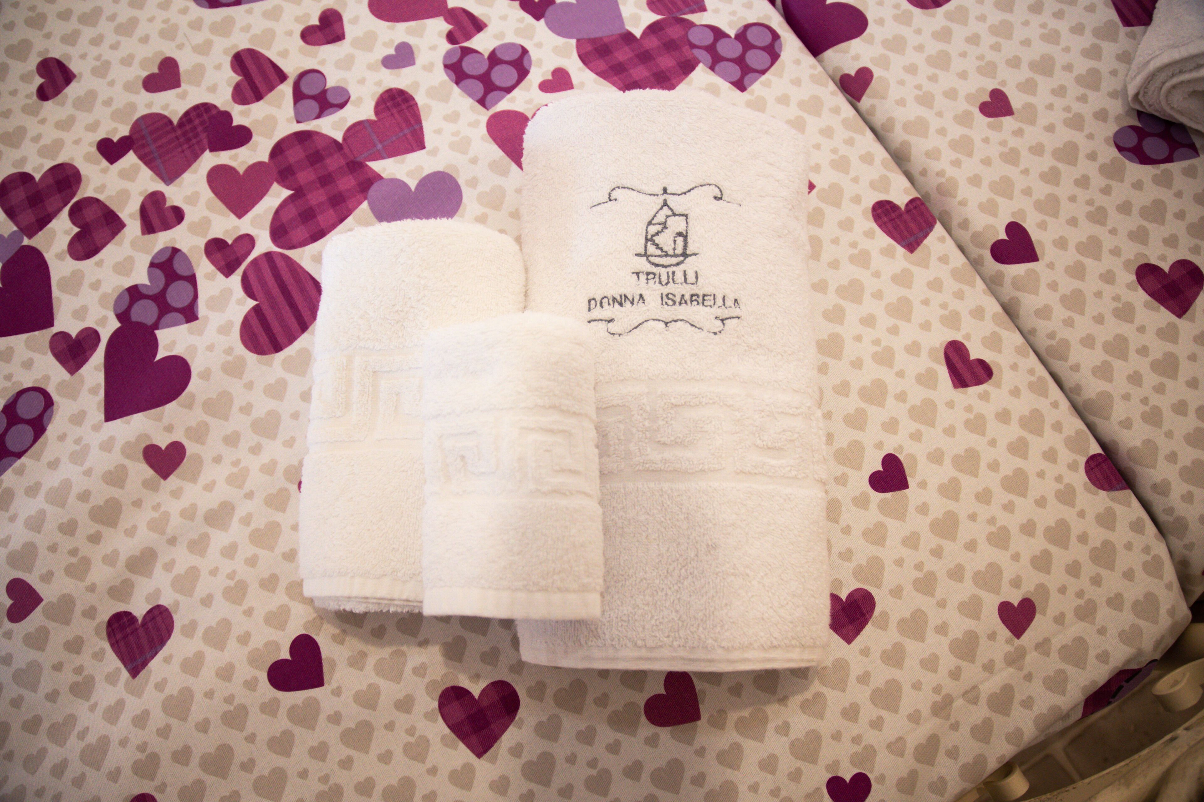 A neatly folded set of white towels with a logo and text on them, placed on a surface with a pattern of hearts.