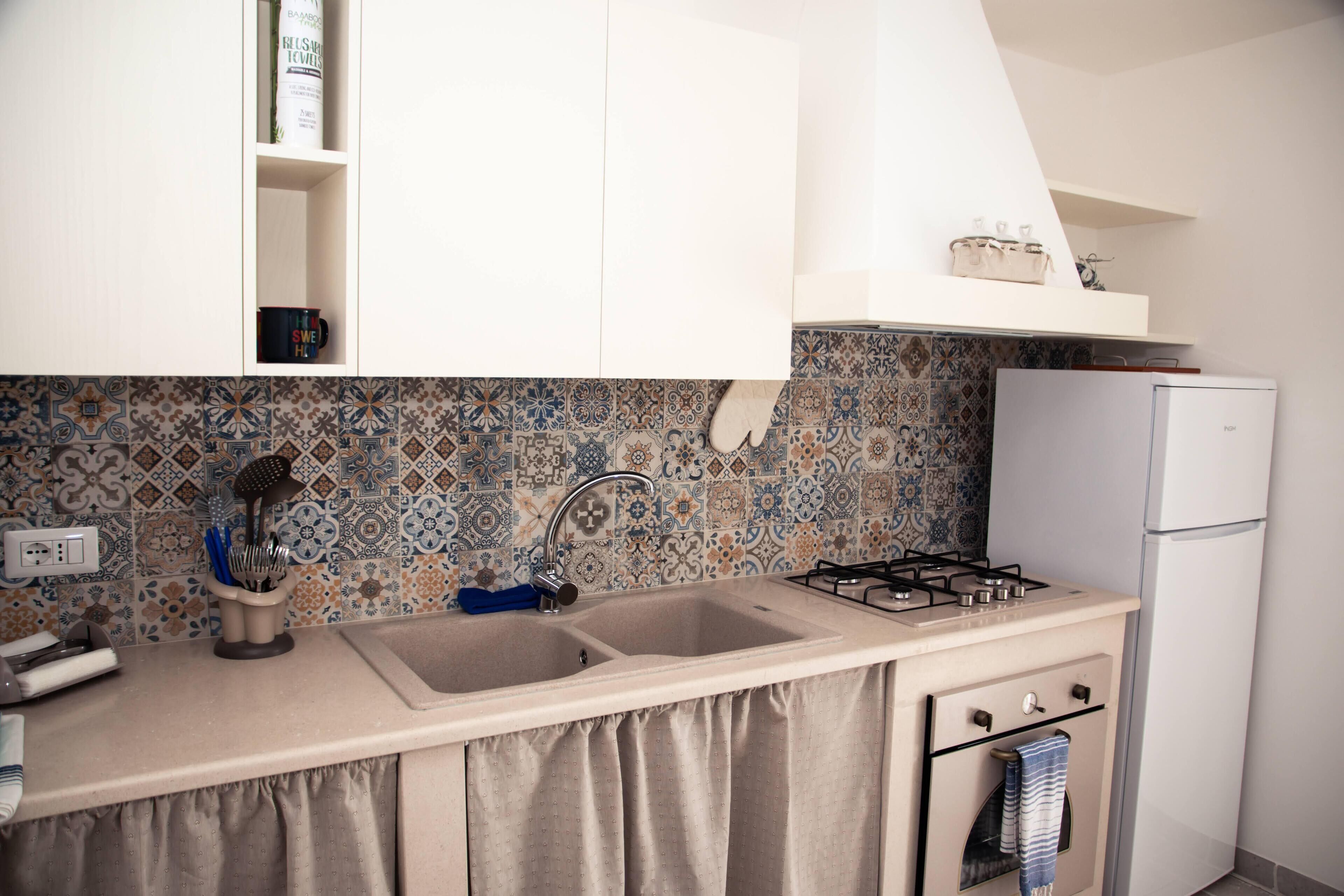 Una cocina con un lavamanos doble, una estufa a gas, un refrigerador blanco y salpicadero de azulejos.