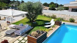 A poolside area with a sun lounger, a covered umbrella, and a small tree. - Trulli Donna Isabella (Locorotondo)