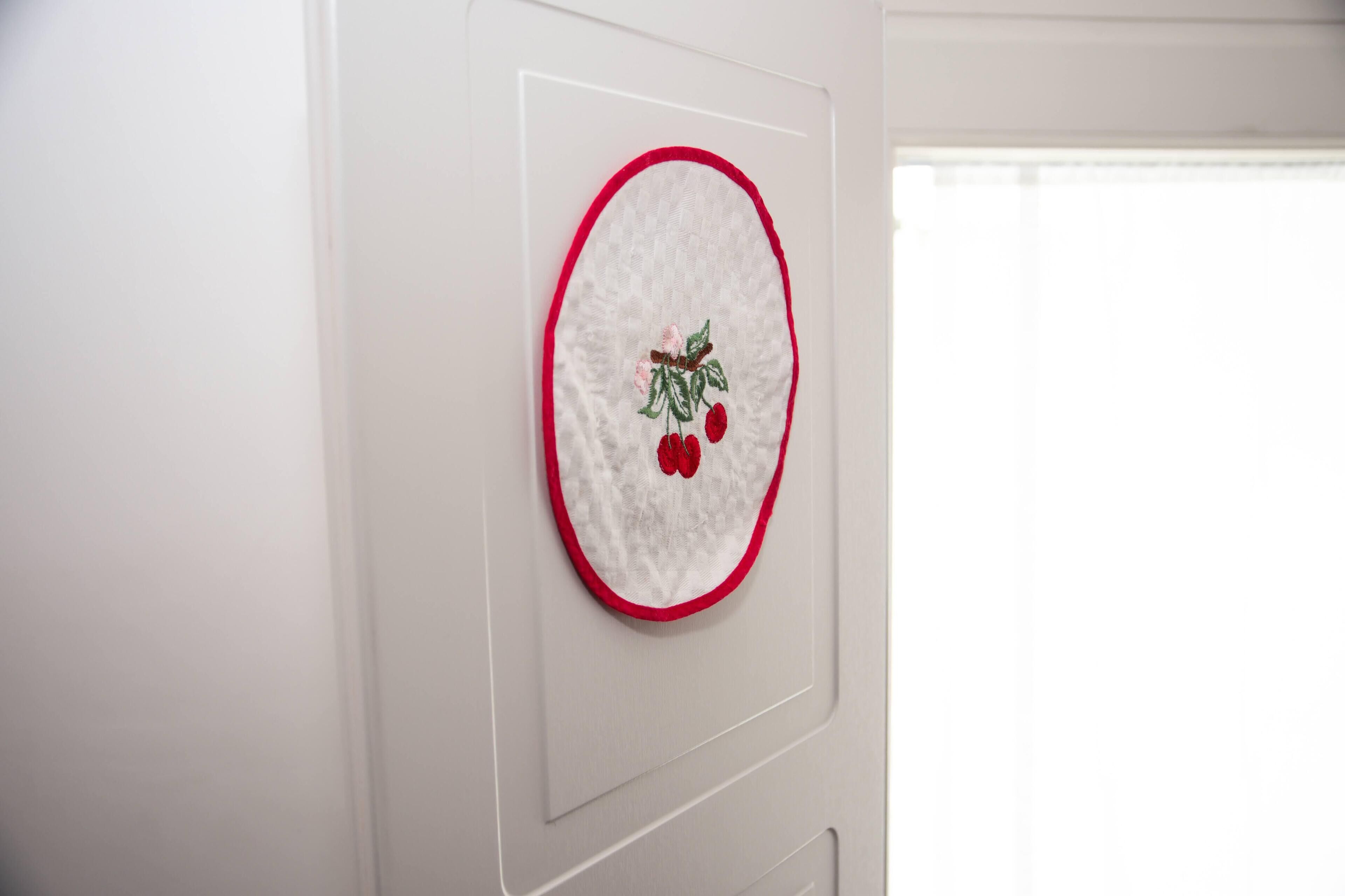 A wall-mounted embroidery of a cherry branch with cherries and a leaf.