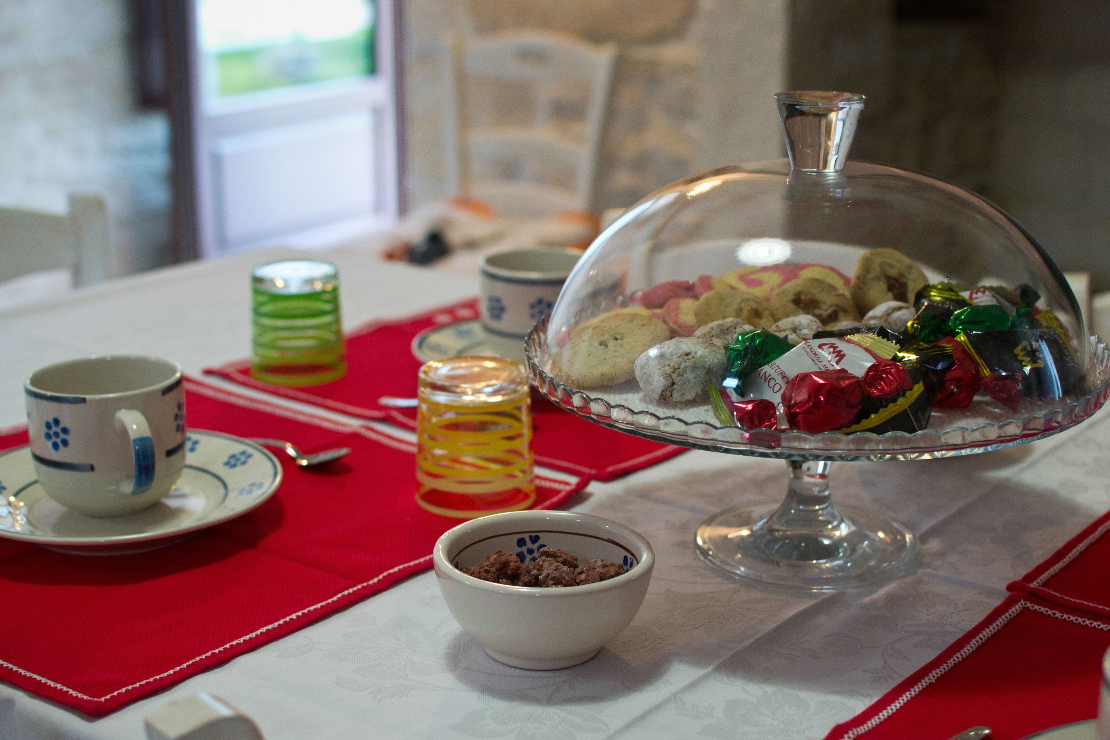 A table with a glass dome dessert stand, a cup, a small bowl, and a candle.