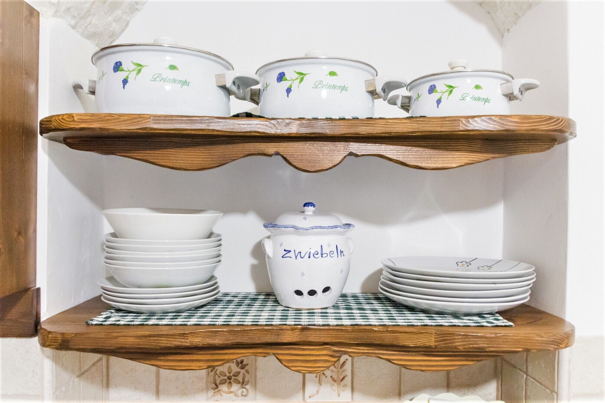 A kitchen shelf with white ceramic kitchenware, including pots, a jug, and stacked plates.