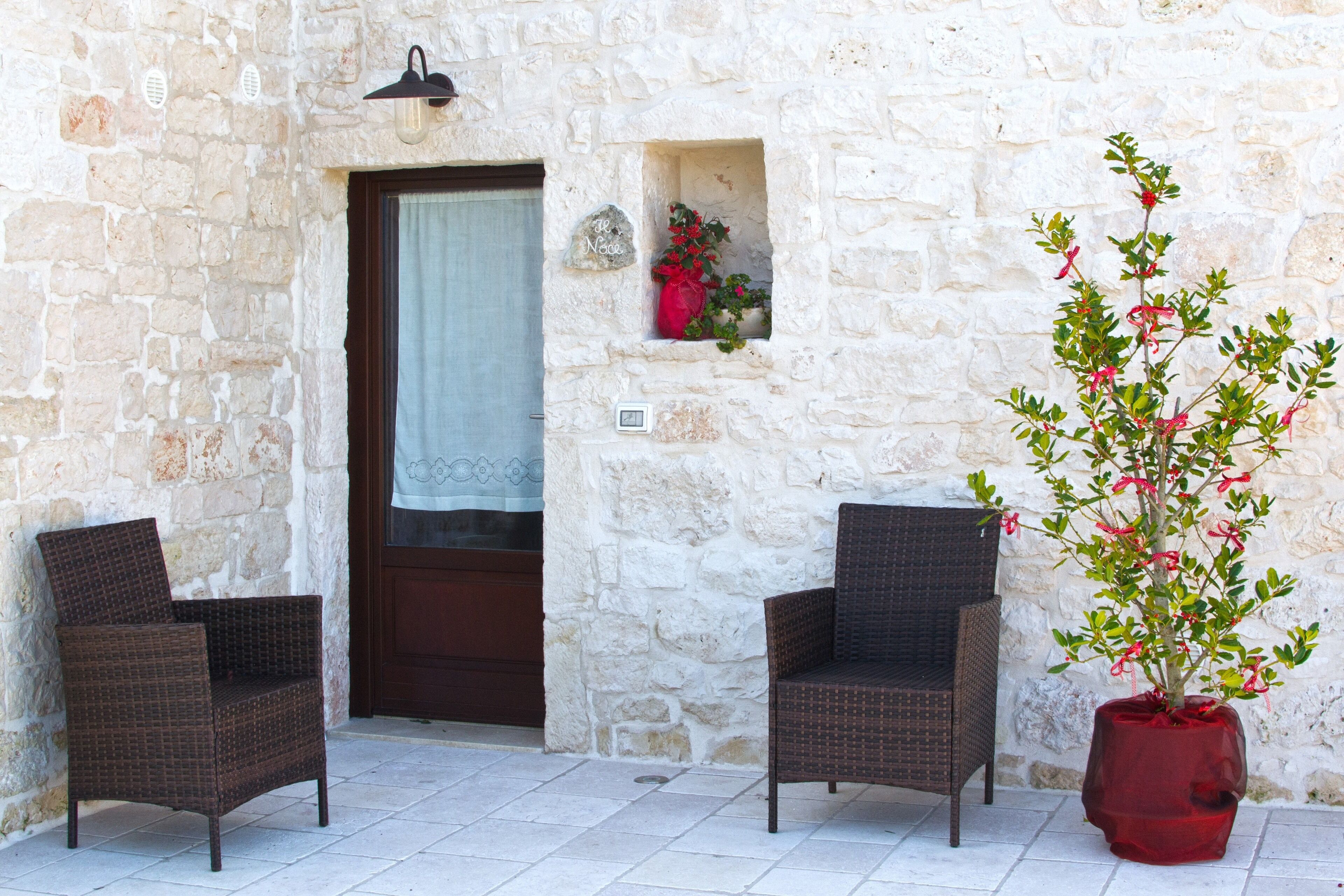 A stone building with two wicker chairs outside a door with a curtain.