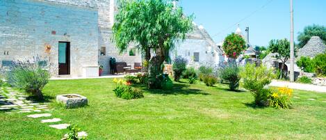 Un bâtiment en pierre avec un jardin devant, comprenant un arbre et diverses plantes.