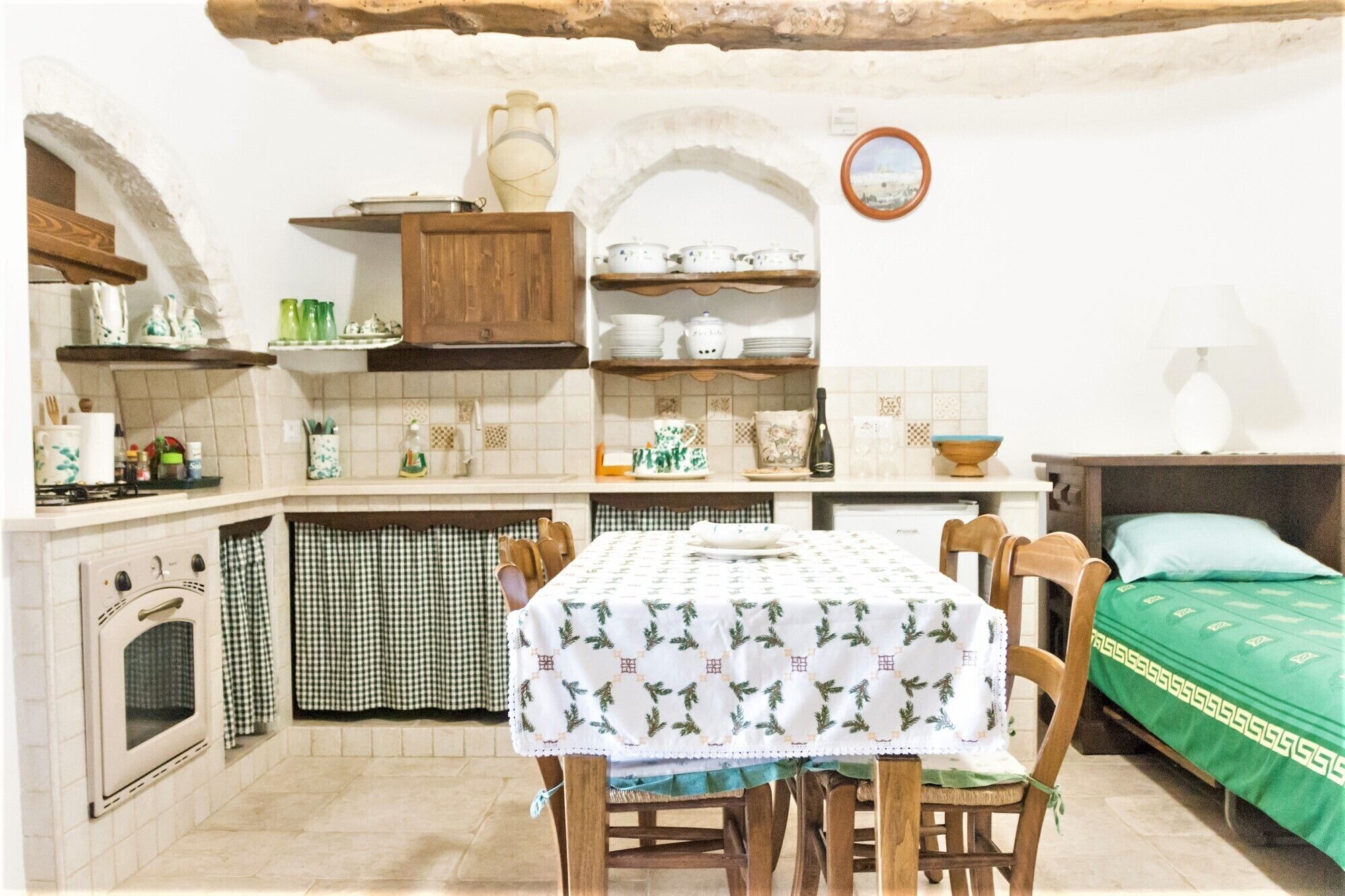 Una cocina compacta con mesa, sillas, horno pequeño y cama con colcha verde.