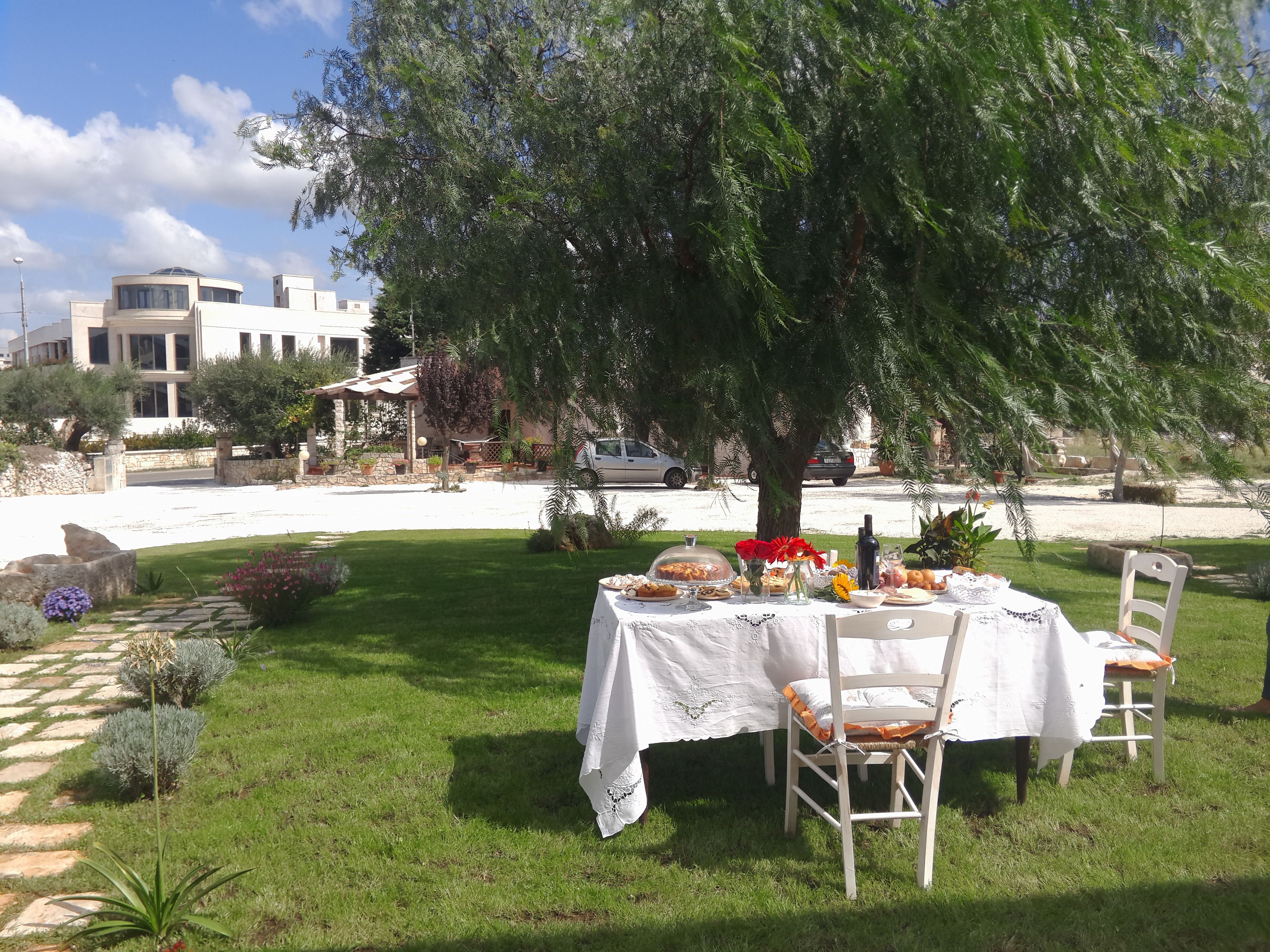 An outdoor dining area with a table set under a tree, surrounded by a well-maintained lawn and a stone pathway.